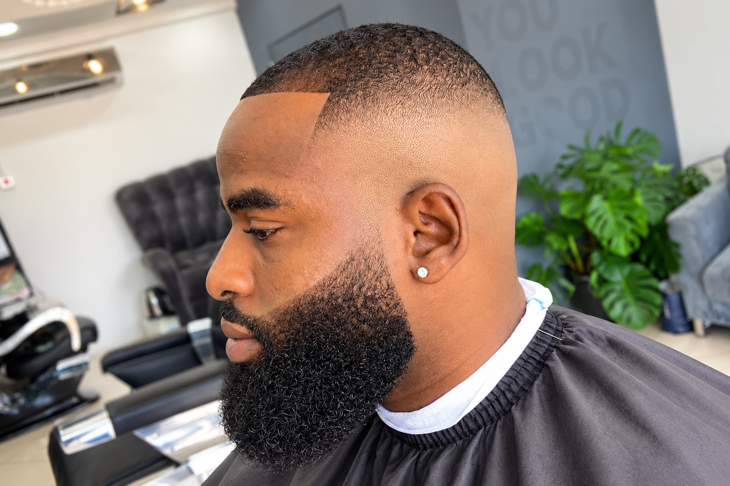 Bald fade with a sharp line-up and a full, shaped beard, side profile in the shop in East Legon