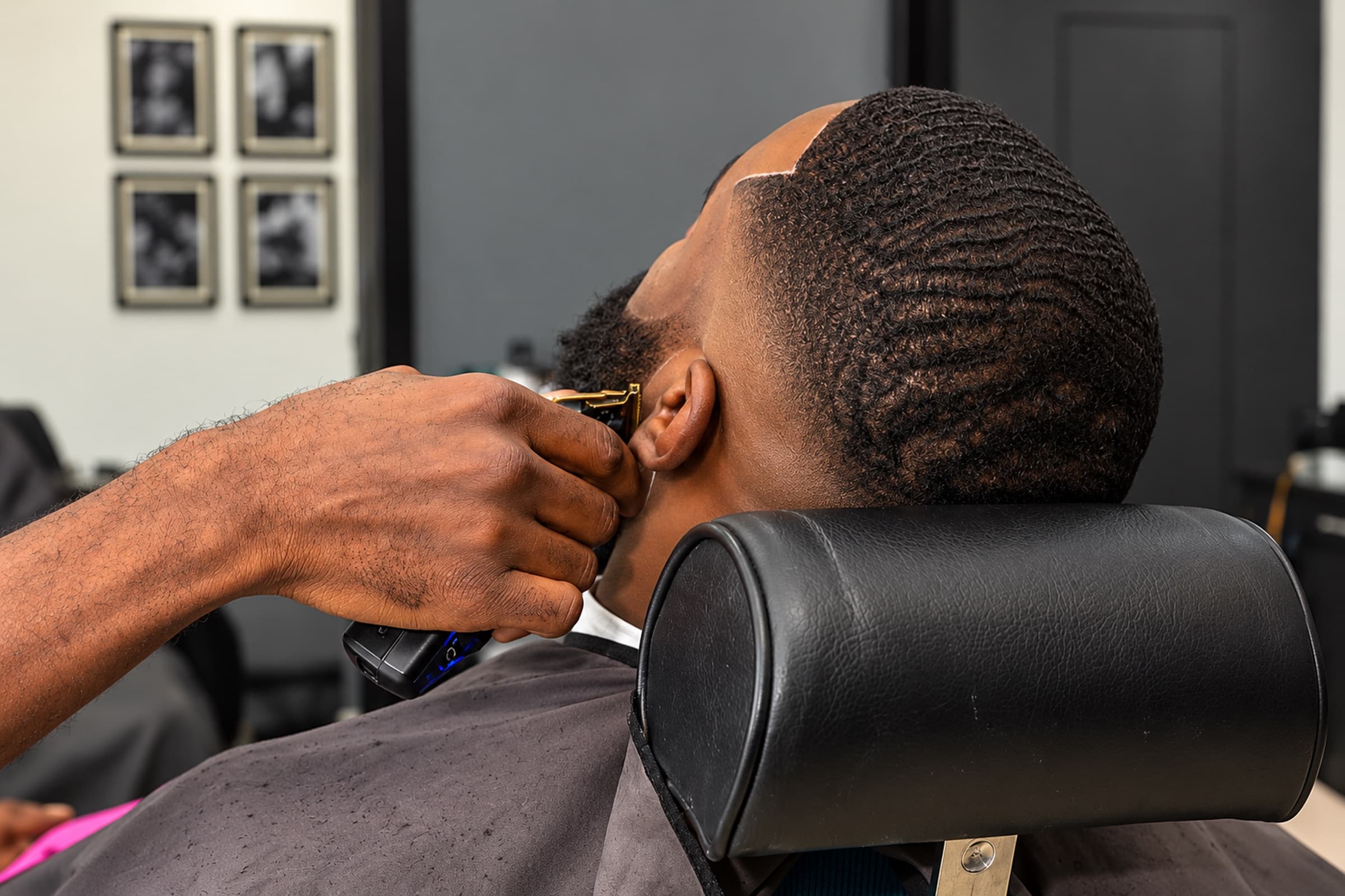 Barber lining up the beard on a client with 360 waves, seen from behind the chair
